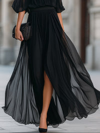 Robe longue noire en mousseline, jupe plissée ample avec fente et ourlet volanté.