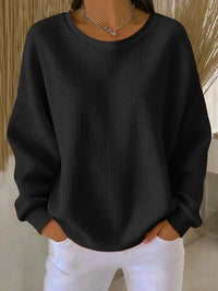 Sweat minimaliste noir en tissu texturé, encolure ronde, manches longues amples.