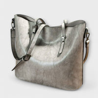 Sac à bandoulière vintage en cuir gris, bandoulière avec attaches, fermeture zippée visible.