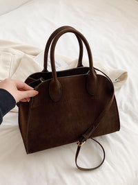 Sac en daim brun avec deux anses et bandoulière, fermeture à fermoir visible