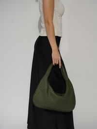 Sac d’épaule Samara tressé vert sauge, tenu à la main avec anses longues.