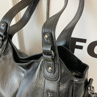Sac cabas en cuir noir, détail des anses et poche zippée sur le devant.