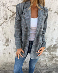 Blazer à carreaux bleu-gris, manches longues, col ouvert et poches passepoilées.