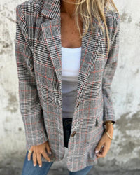 Blazer à carreaux gris, lignes rouges, manches longues, col en pointe et poches.