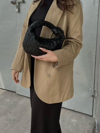 Sac à anse mini tressé noir en tresse, porté contre le manteau, ouverture en haut.