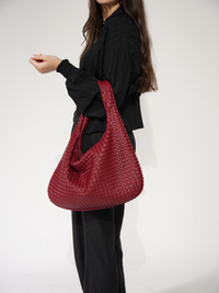 Sac d’épaule rouge vin tressé, porté à l’épaule, anses courtes et ouverture visible.