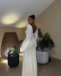 Robe longue blanche en maille ajourée, dos échancré, manches longues évasées.
