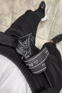 Pantalon noir avec ceinture décorée et inscriptions, coupe ajustée.