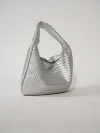 Sac d’épaule argent en tressage, anse courte renforcée, intérieur visible par l’ouverture.
