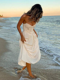 Robe longue blanche bustier sans bretelles plissée, porté de côté avec fronces.