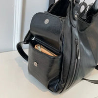 Sac cabas en cuir noir, porté main, poches latérales et compartiment zippé.
