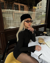 Robe noire à col montant et manches longues, portée avec béret noir et lunettes