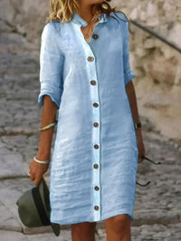 Robe midi bleu clair en lin, col chemise, patte boutonnée, manches retroussées.