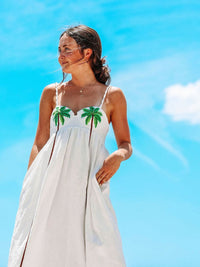 Robe longue blanche à fines bretelles et motifs palmiers verts, vue de profil.