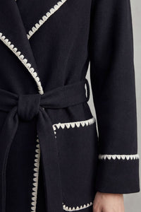 Manteau long noir : ceinture nouée et bordure contrastante autour des poches