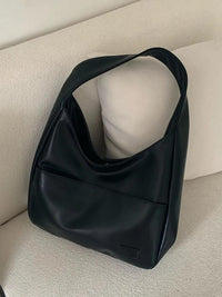 Sac porté épaule noir avec petite étiquette rectangulaire, anse courte.
