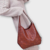Sac vintage en cuir brun, anses longues, aspect patiné, poche extérieure sur le devant