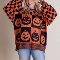 Pull col rond à motif citrouilles orange, bas et poignets marron, manches à carreaux.