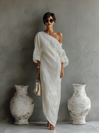 Robe longue fluide ivoire à une épaule, manches amples, coupe longue et aérienne.