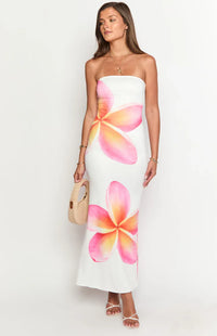 Robe longue blanche sans bretelles, imprimé fleurs rose et mauve, pochette beige en main.