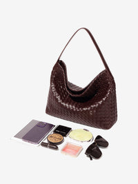 Sac cabas tressé bordeaux posé, anses longues en cuir, ouverture en forme d’entonnoir.