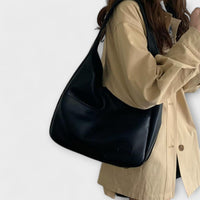 Sac à bandoulière en cuir noir, forme arrondie avec poche rectangulaire plaquée.
