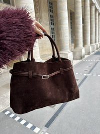 Sac en daim marron tenu à la main, fermeture à boucle métallique centrale.