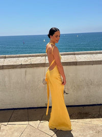 Robe longue dos nu jaune à bretelles croisées, portée sur le côté