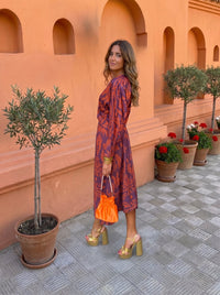 Robe midi imprimée rouge-orangé, manches longues, décolleté noué et ceinture.