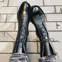 Bottes noires à lacets croisés et bout pointu, vue des chaussures posées.