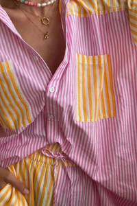 Chemise rayée rose et jaune, col boutonné, lien à nouer, poche carrée devant.
