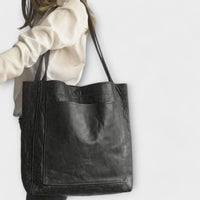 Sac à main noir avec poche frontale et anses renforcées.