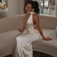 Robe longue en satin blanc, encolure halter, décolleté en V, drapé léger sur la taille.
