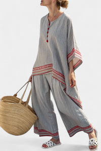 Blouse asymétrique en tissu gris bleuté, encolure en V et liserés rouges rayés.