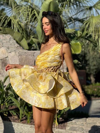 Robe courte jaune fleurie à une épaule, volants évasés et liens de fronce à la taille.