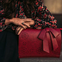 Sac cartable rouge en cuir, motifs ajourés et grand ruban noué sur la face avant