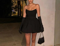 Robe courte ballon noire à encolure cœur, jupe plissée et gants longs.