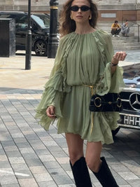 Robe courte vert clair à volants superposés, encolure ronde, portée avec bottes noires.
