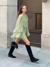 Robe courte fluide vert clair à volants, encolure ronde, portée avec bottes hautes.