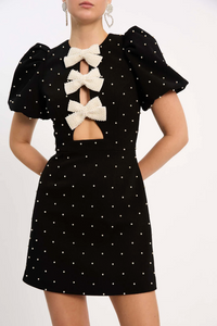 Robe courte noire à pois blancs, manches bouffantes et nœud beige au col
