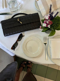 Sac tressé noir avec rabat et fermoir doré, posé sur table