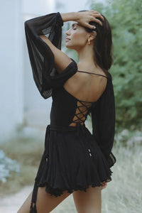 Mini-robe noire dos nu à laçage croisé, manches longues transparentes et jupe froncée.