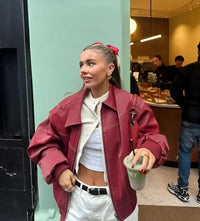 Veste en cuir oversize rouge avec col rabattu, poche zippée et surpiqûres claires.