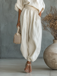 Ensemble deux pièces ivoire : haut drapé asymétrique et pantalon ample à taille froncée.