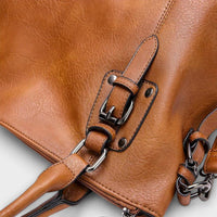 Sac marron : sangle et boucle avec anneaux chromés, couture visible.