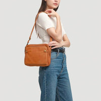 Sac à main en cuir orange, porté en bandoulière sur l’épaule, fermeture zippée.