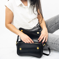 Sac porté épaule noir avec rabat, boutons dorés et bandoulière noire.