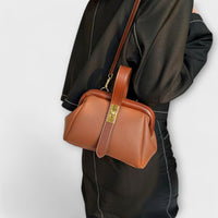 Sac rétro en cuir grainé marron cuivré, bandoulière longue et fermeture à plaque dorée.