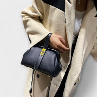 Sac rétro en cuir grainé bleu marine, bandoulière noire et plaque dorée centrale.