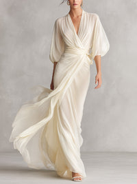 Robe longue ivoire transparente à col V, manches bouffantes, drapée et ceinture nouée.